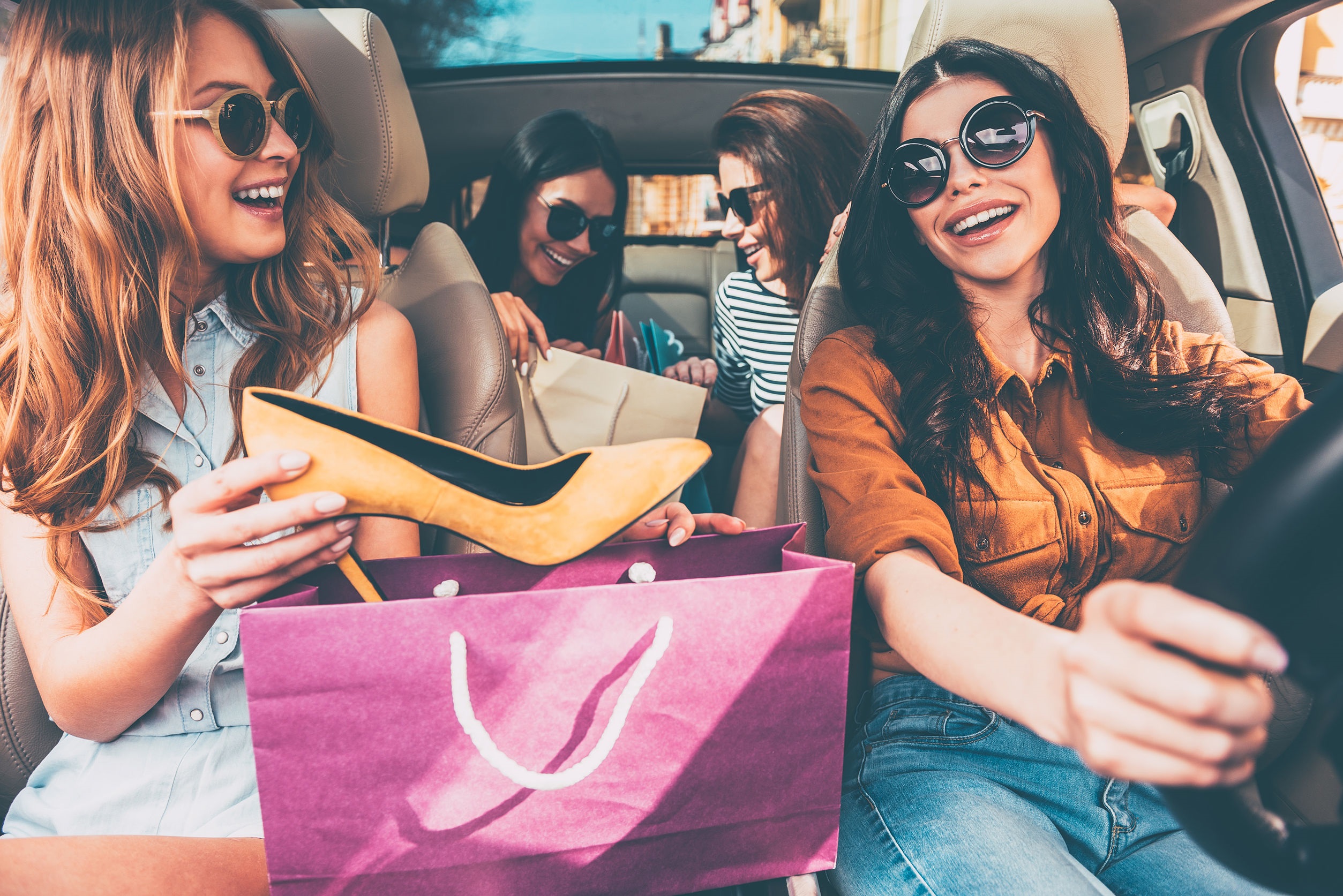Next stop is lingerie shop! Four beautiful young cheerful women holding  shopping bags and looking at each other with smile while sitting in car -  The Shops at Hilltop